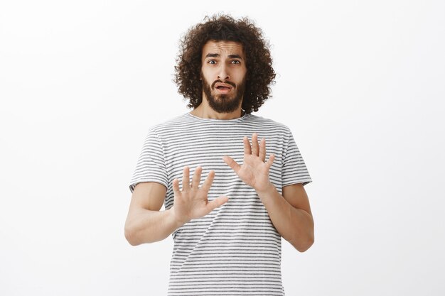 Portrait of embarrassed cute hispanic boyfriend with beard, being surprised with unexpected offer, raising palms in no or rejection gesture, trying to deny something or refuse