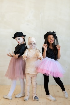 Portrait of emotional multi-ethnic kids in costumes of mimes and mummy making scaring gestures at halloween party