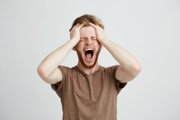 Portrait of emotional upset angry man shouting screaming holding head.