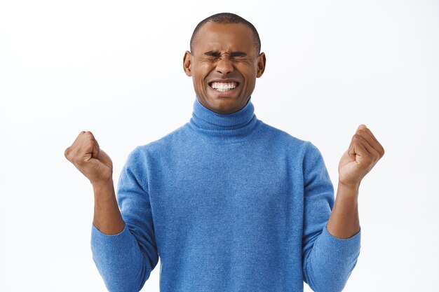 Portrait of encouraged young african american man boosting confidence, fist pump, close eyes and smiling, motivating himself stay positive