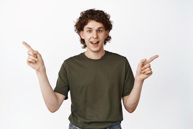 Portrait of enthusiastic curly man pointing fingers sideways showing two ways variants standing happy against white background