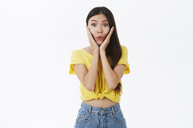 Portrait of enthusiastic excited and intrigued charming female shopoholic in yellow trendy t-shirt folding lips