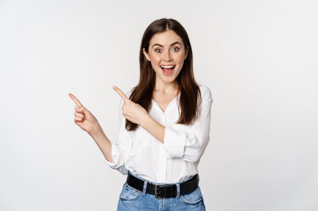 Portrait of enthusiastic smiling woman female entrepreneur pointing fingers left and showing adverti...