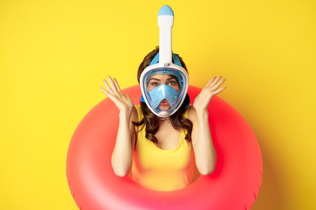 Portrait of enthusiastic young woman on vacation wearing snorkling diving mask and swimming ring sta...