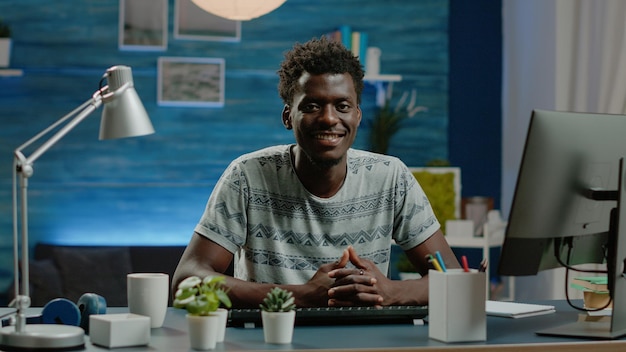 Portrait of entrepreneur prepared for remote work on computer at desk. Corporate employee looking at camera and smiling, working from home using technology. Business worker in workspace