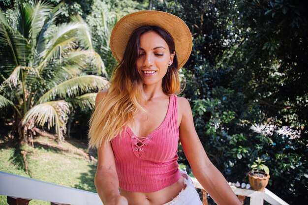 Portrait of european fit slim pretty woman without make up, natural light, with long hair, pink summer top and straw hat