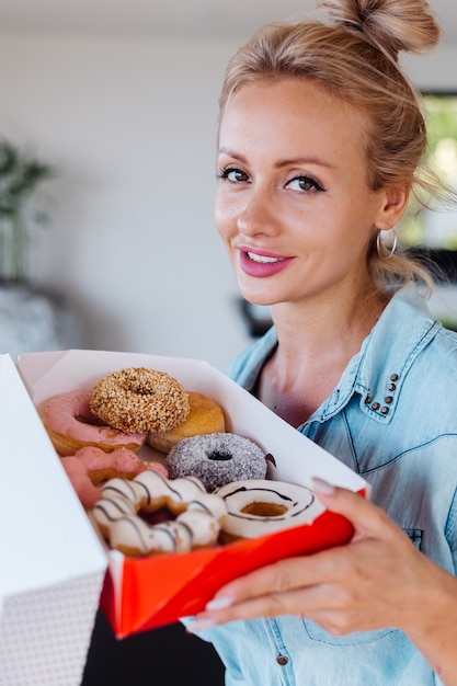 Free photo portrait of european woman with blonde hair enjoying donuts in kitchen at home villa.