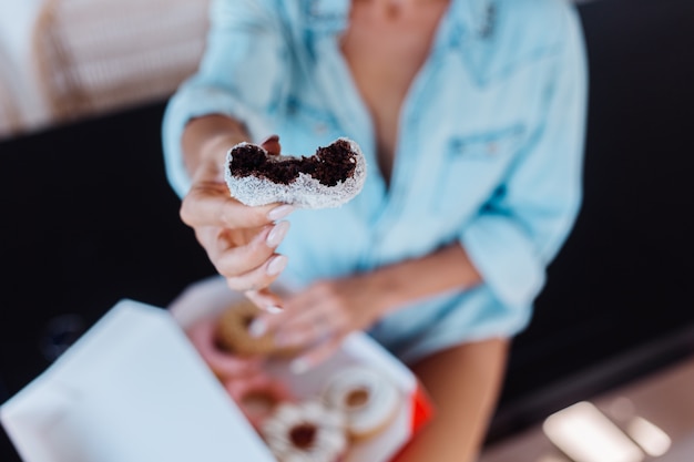 Portrait of european woman with blonde hair enjoying donuts in kitchen at home villa.