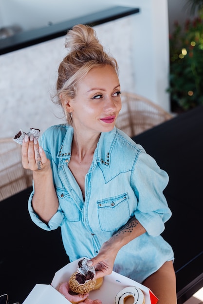 Portrait of european woman with blonde hair enjoying donuts in kitchen at home villa.