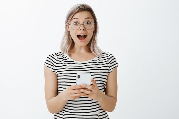 Portrait of excited blonde girl posing in the studio with her phone