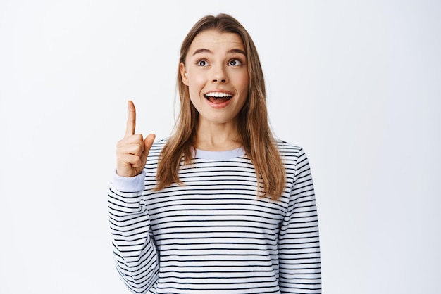 Portrait of excited female student smiling amused pointing and looking up with dreamy happy face checking out cool advertisement white background