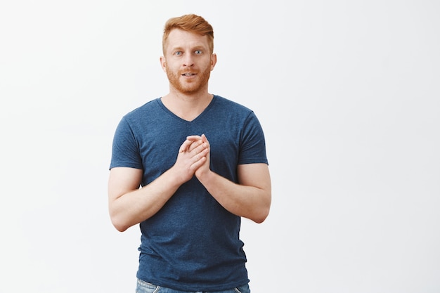 Portrait of excited and intrigued good-looking businessman with ginger hair and bristle touching palms near chest and smiling with curious expression