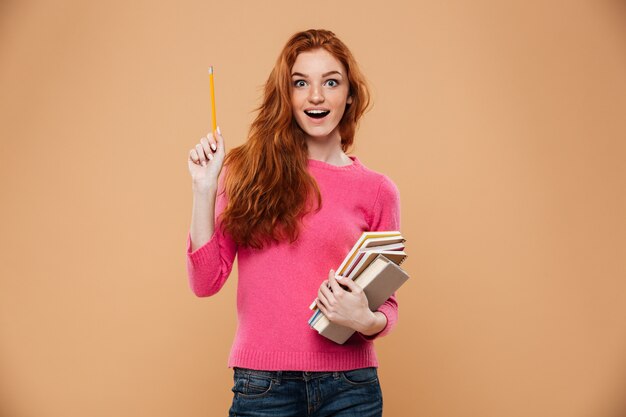 Portrait of an excited pretty redhead girl holding books and having an idea