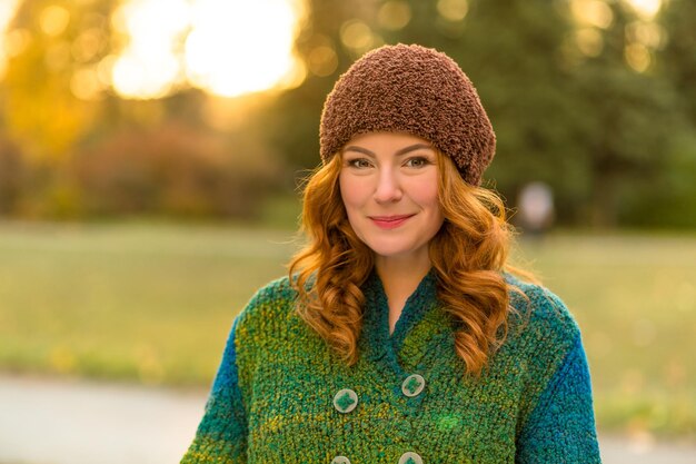 笑顔で写真家のためにポーズをとって興奮した赤毛の女性の肖像画秋の公園を歩いて茶色の帽子をかぶった幸せな美しい女性