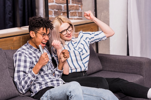 Portrait of excited teenage couple sitting on sofa clenching their fist