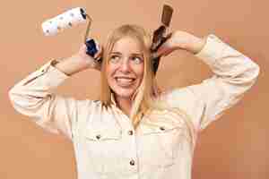 Free photo portrait of excited young caucasian woman holding paintbrush and roller while painting walls in her bedroom