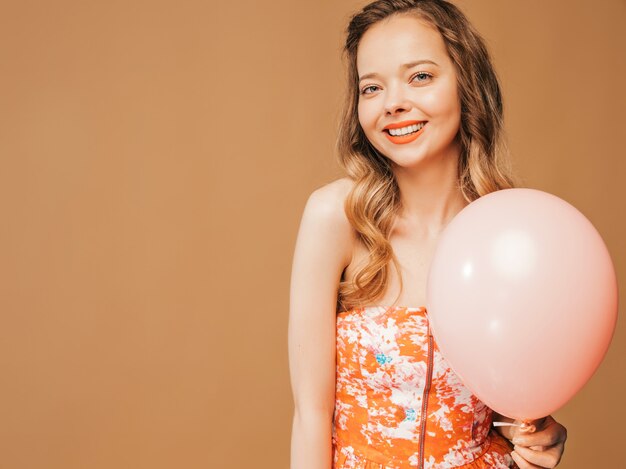 Portrait of excited young girl posing in trendy summer colofrul dress. Smiling woman with pink balloon posing. Model ready for party