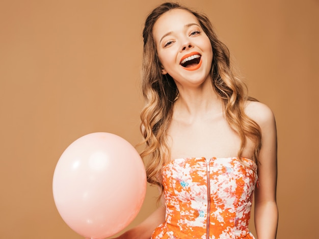 Portrait of excited young girl posing in trendy summer colorful dress. Smiling woman with pink balloon posing. Model ready for party