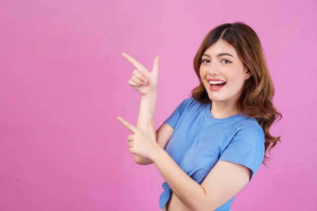 カジュアルなTシャツを着て興奮している若い女性の肖像画は、ピンクの背景に分離されたオファー広告のプロモーションをデモンストレーションします。