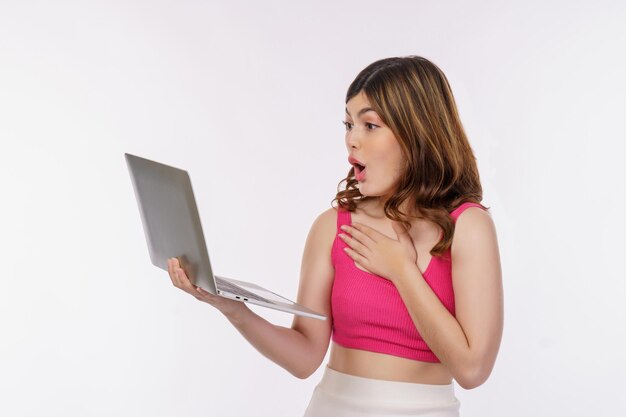 흰색 배경 위에 격리된 노트북 컴퓨터에서 작업하는 흥분된 젊은 여성의 초상화