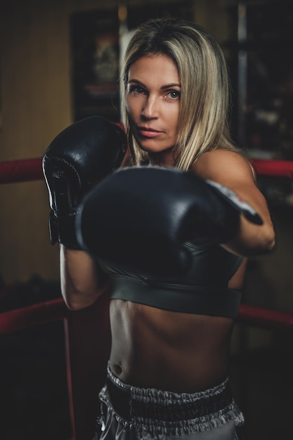 Портрет опытной боксерши в боксёрских перчатках и спортивной одежде.