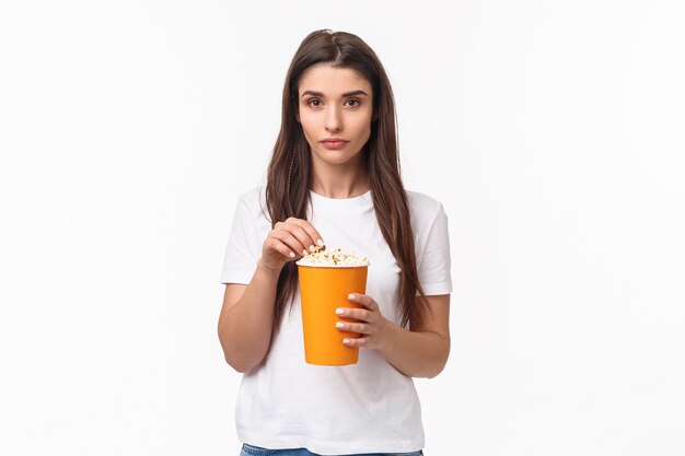 Портрет выразительной молодой женщины ест попкорн
