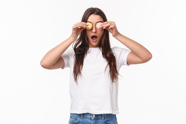 portrait expressive young woman holding tasty two macarons over eyes