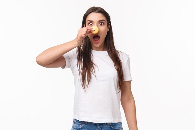 portrait expressive young woman holding tasty two macarons over eyes