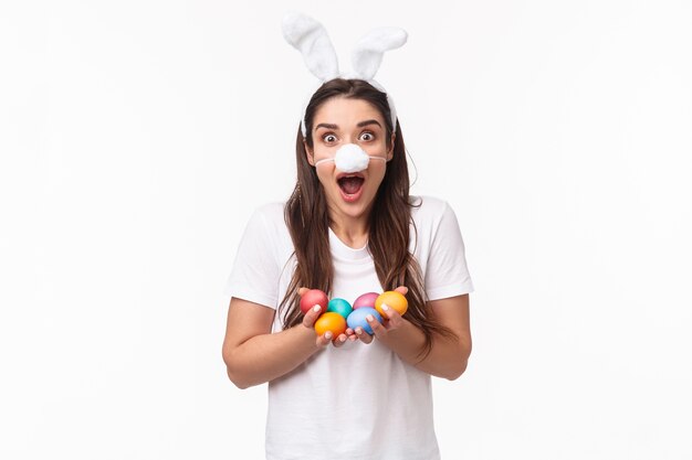 portrait expressive young woman wear rabbit ears and nose, holding colored eggs