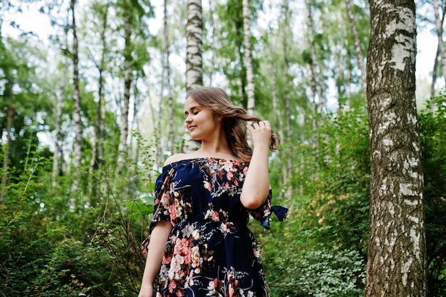 숲이나 공원에서 포즈를 취하는 세련된 곱슬머리를 한 예쁜 드레스를 입은 멋진 어린 소녀의 초상화