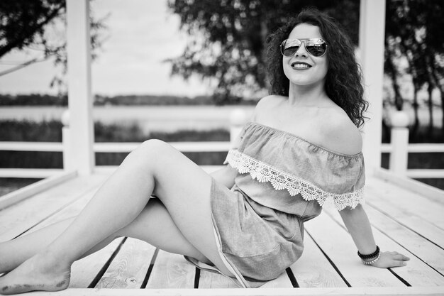 Portrait of a fabulous young girl wearing chic outfit posing on a white wooden terrace Black and white photo