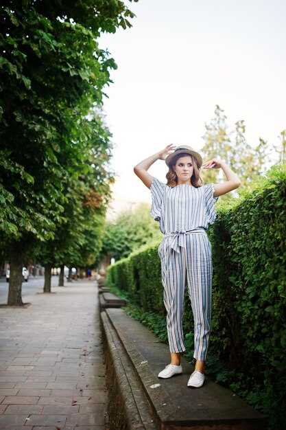 Portrait of a fabulous young woman in striped overall walking on the barrier in the park