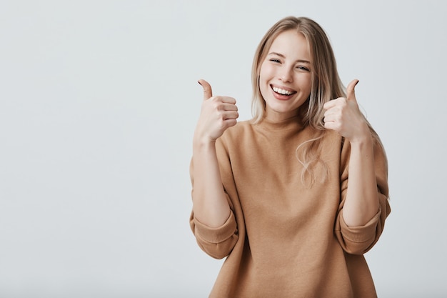 Portrait of fair-haired beautiful female woman with broad smile and thumbs up