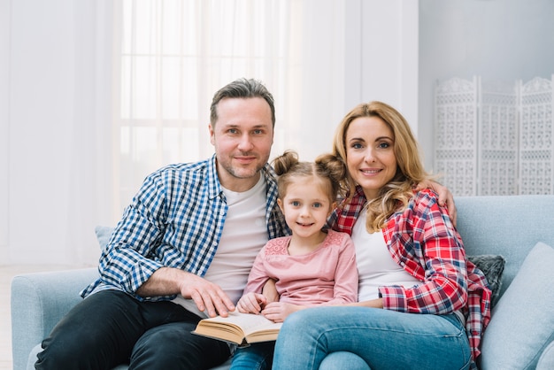 Free photo portrait of family reading book together sitting on sofa