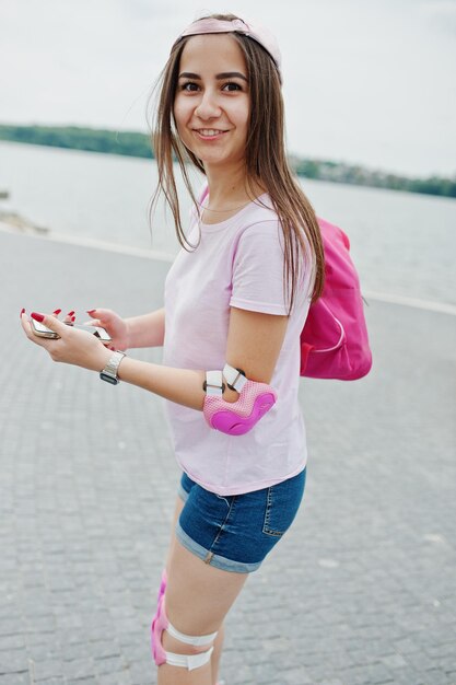 湖の隣の公園で彼女の手で彼女の携帯電話でローラースケートをする幻想的な若い女性の肖像画