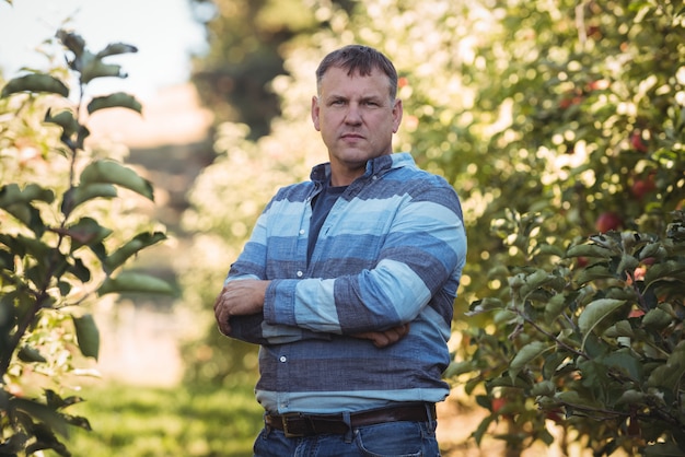 Портрет фермера, стоя с оружием, пересекли в яблоневом саду