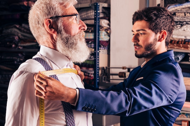 Free photo portrait of a fashion designer taking measurement of his customer's chest in his workshop