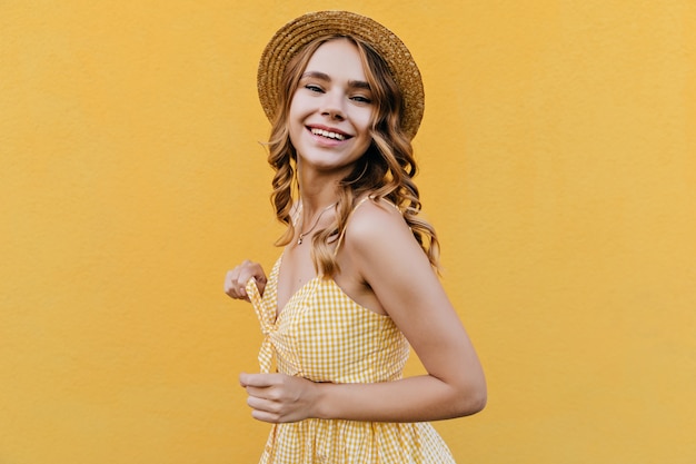 Portrait of fashionable curly woman smiling. Indoor shot of cute female model in retro dress and hat.