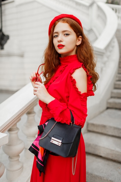 Free photo portrait of fashionable ginger female in red beret and elegant dress posing outdoor.