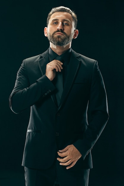 Portrait of a fashionable young man with stylish haircut wearing trendy suit posing over black.