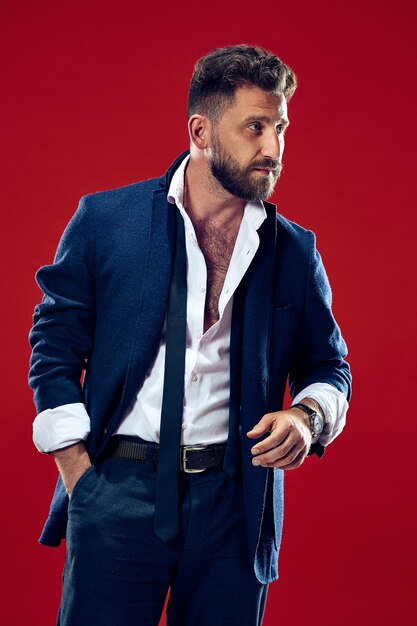 Portrait of a fashionable young man with stylish haircut wearing trendy suit posing over red.