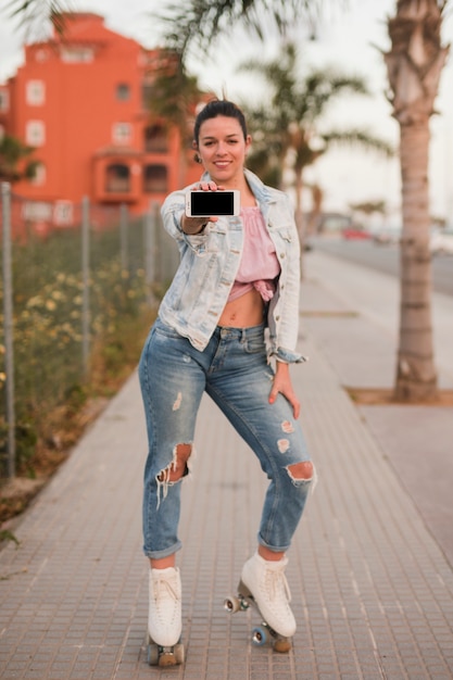 Portrait of a fashionable young woman standing on sidewalk showing mobile phone