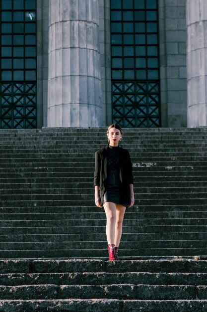 Portrait of a fashionable young woman standing on staircase looking at camera