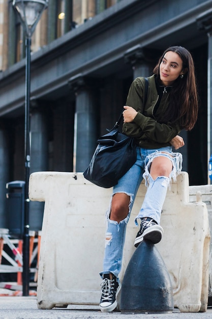 Portrait of a fashionable young woman with bag sitting on street