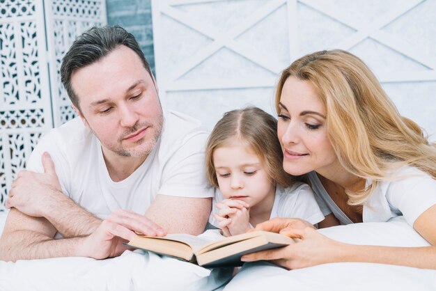 Portrait of father; mother and daughter reading book on bed