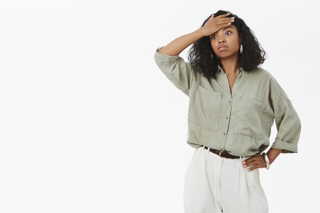 Portrait of fed up tensed and exhausted cute dark-skinned businesswoman in blouse and pants holding hand on waist exhaling