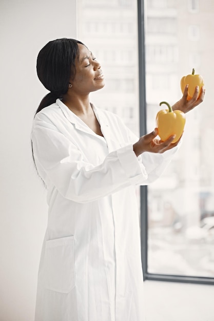 Portrait of female black doctor standing and holding red and yellow peppers