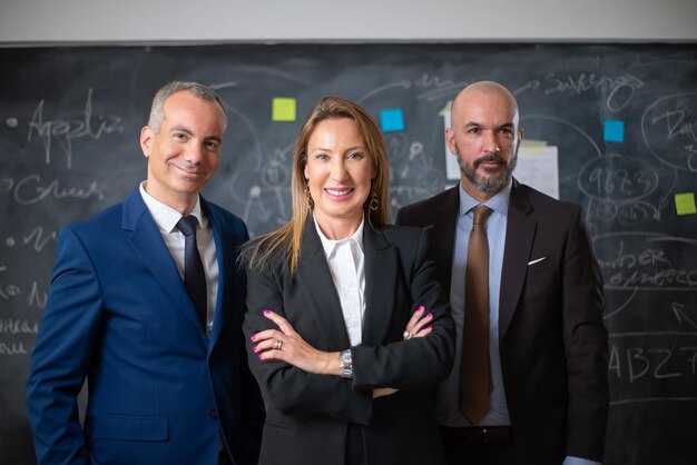 Portrait of female business leader and her colleagues. Two cheerful men and woman standing together after corporate meeting in office, smiling looking at camera. Female leadership in business concept