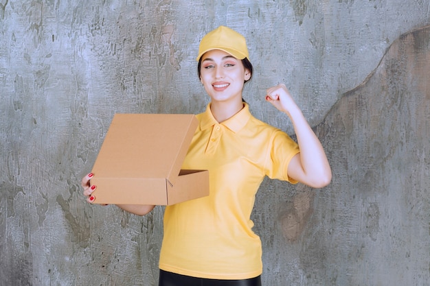 Portrait of female courier holding cardboard box and raising hand