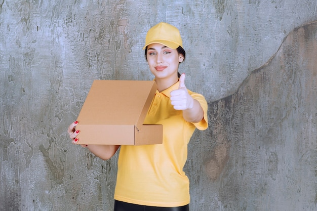 Free photo portrait of female courier holding cardboard box and showing thumb up